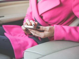 車の中でスマートフォンを見るピンクのコートの女性
