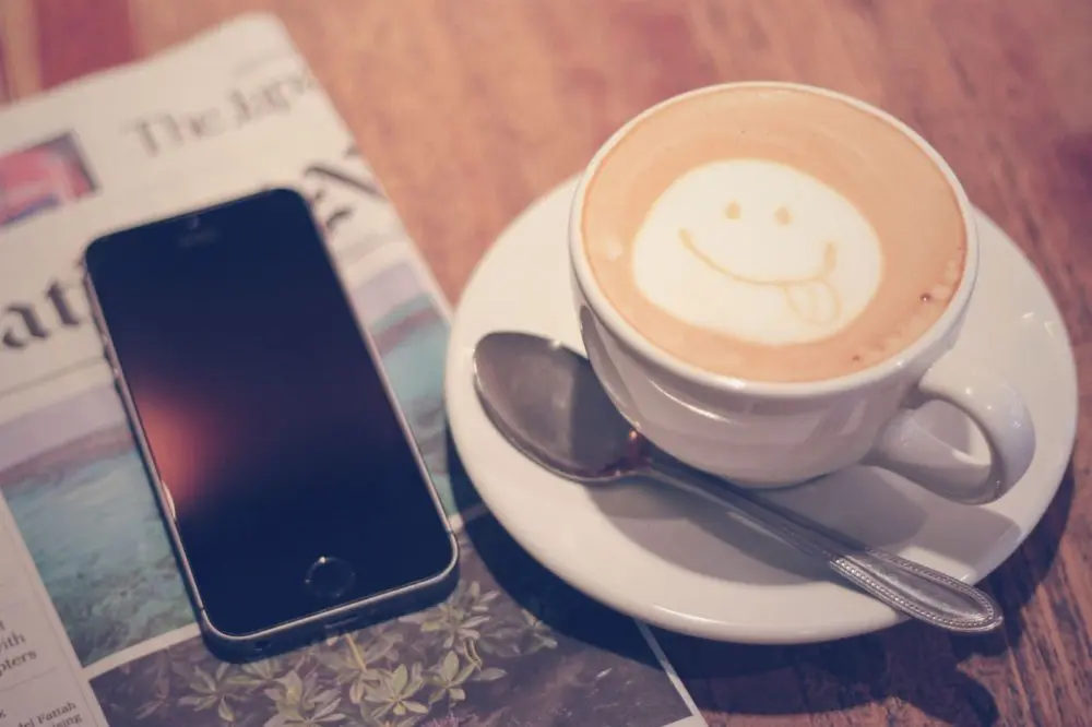 スマイルマークが描かれたカプチーノとスマートフォン