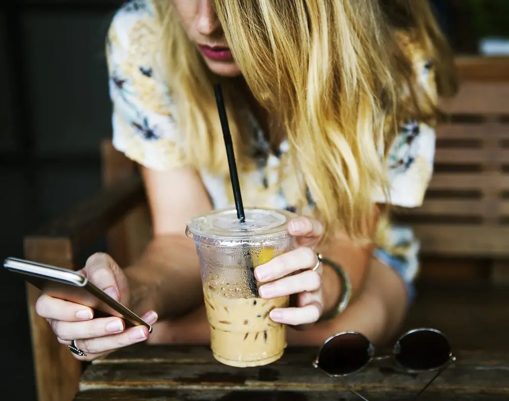 アイスカフェラテ片手にスマホをチェックする女性